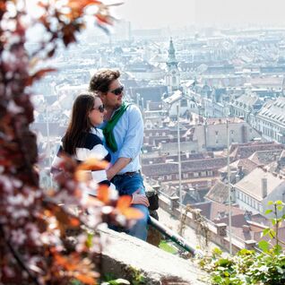 Bild zeigt Paar die den Ausblick auf den Grazer Schlossberg über Graz genießen.