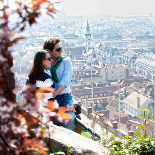 Bild zeigt Paar die den Ausblick auf den Grazer Schlossberg über Graz genießen.