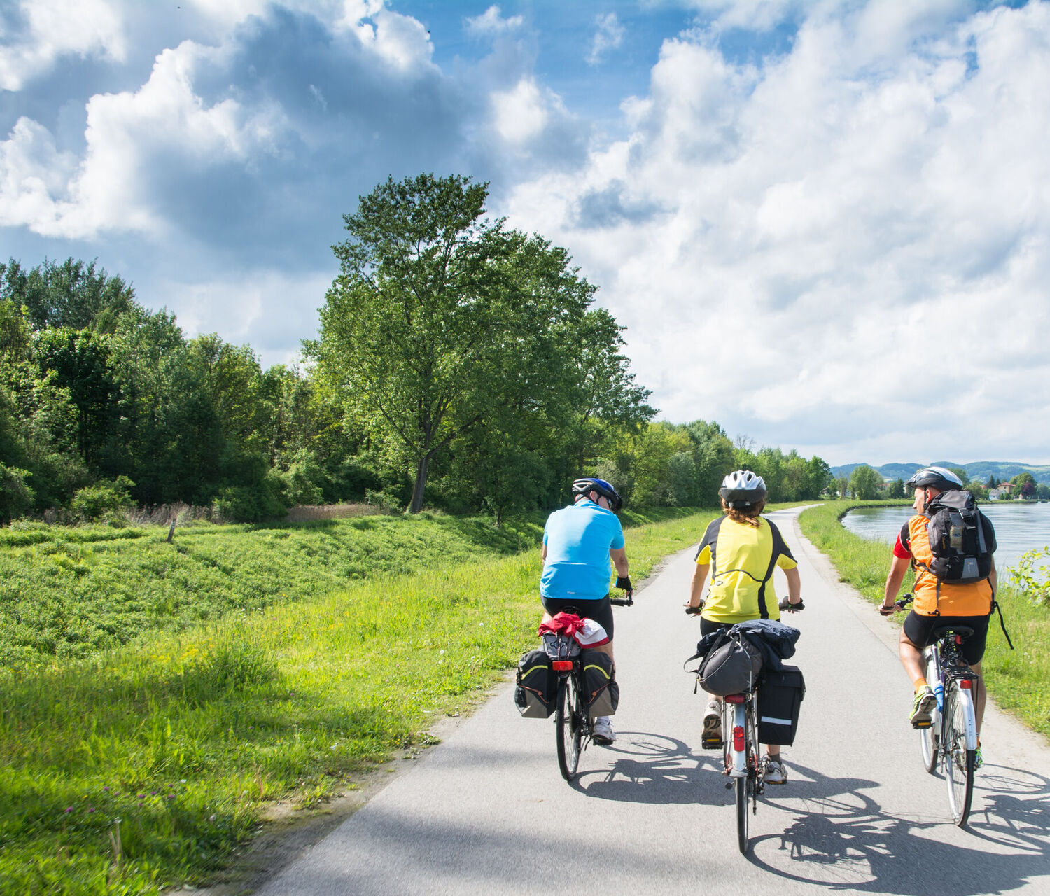 Bild zeigt 3 Fahradfahrer im Grünen auf einem Weg neben einem Fluß.
