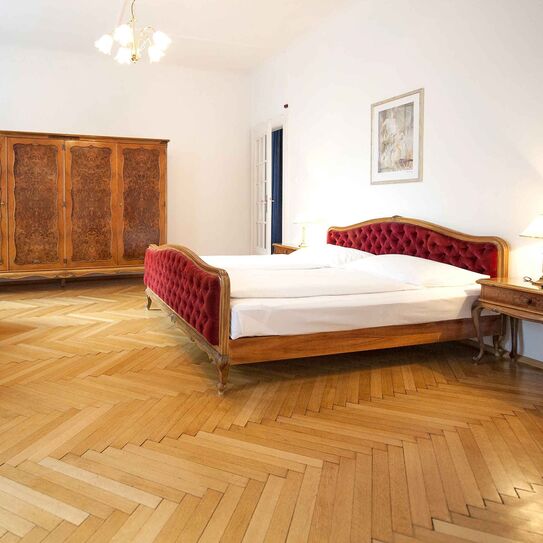 Bild zeigt Hotelsuite mit rotem Samtbett und Holzmöbel im Jugendstil.