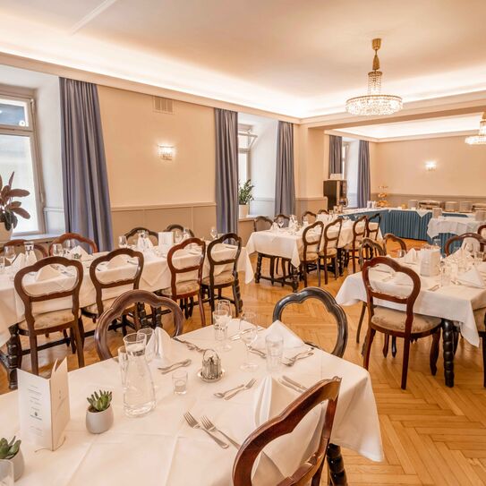 Bild zeigt großen, historischen Raum mit barocken Holzstühlen, vielen eingedeckten Tischen und Kristalllustern. 