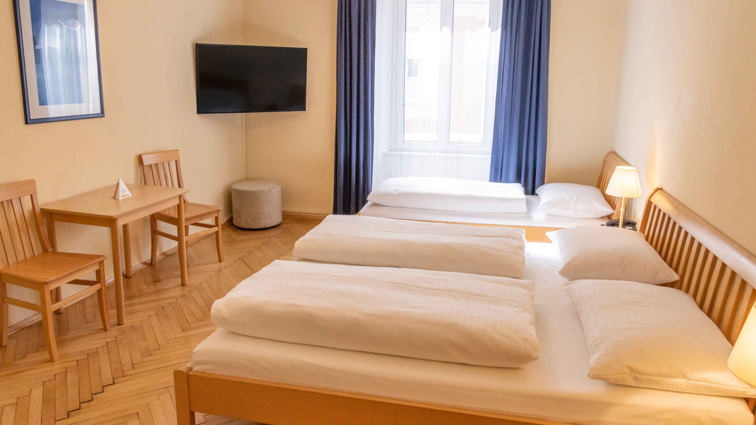 Foto zeigt großzügiges, helles Dreibettzimmer mit Doppelbett und Einzelbett in Holz.