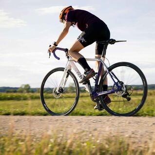 Bild zeigt seitliche Ansicht eines Fahrradfahrers auf einem Wiesenweg.