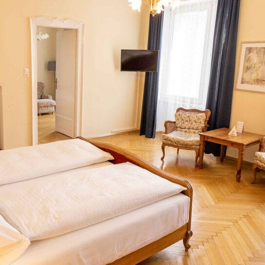 Foto zeigt großzügige Suite mit Blick vom Bett in den Raum mit Mobiliär im Jugendstil.