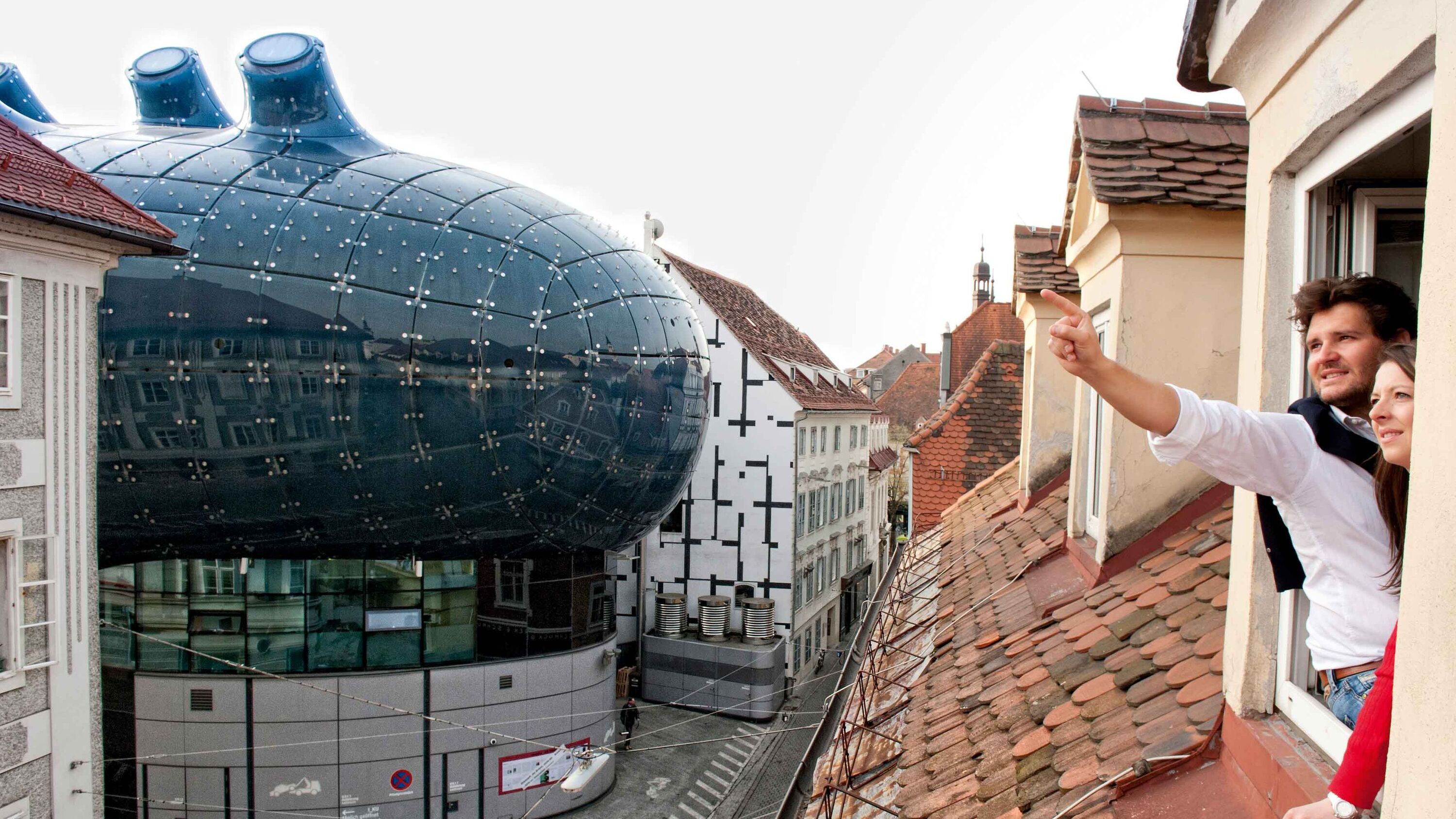 Bild zeigt Mann und Frau aus dem Fenster schauend, mit Blick aufs Grazer Kunsthaus.