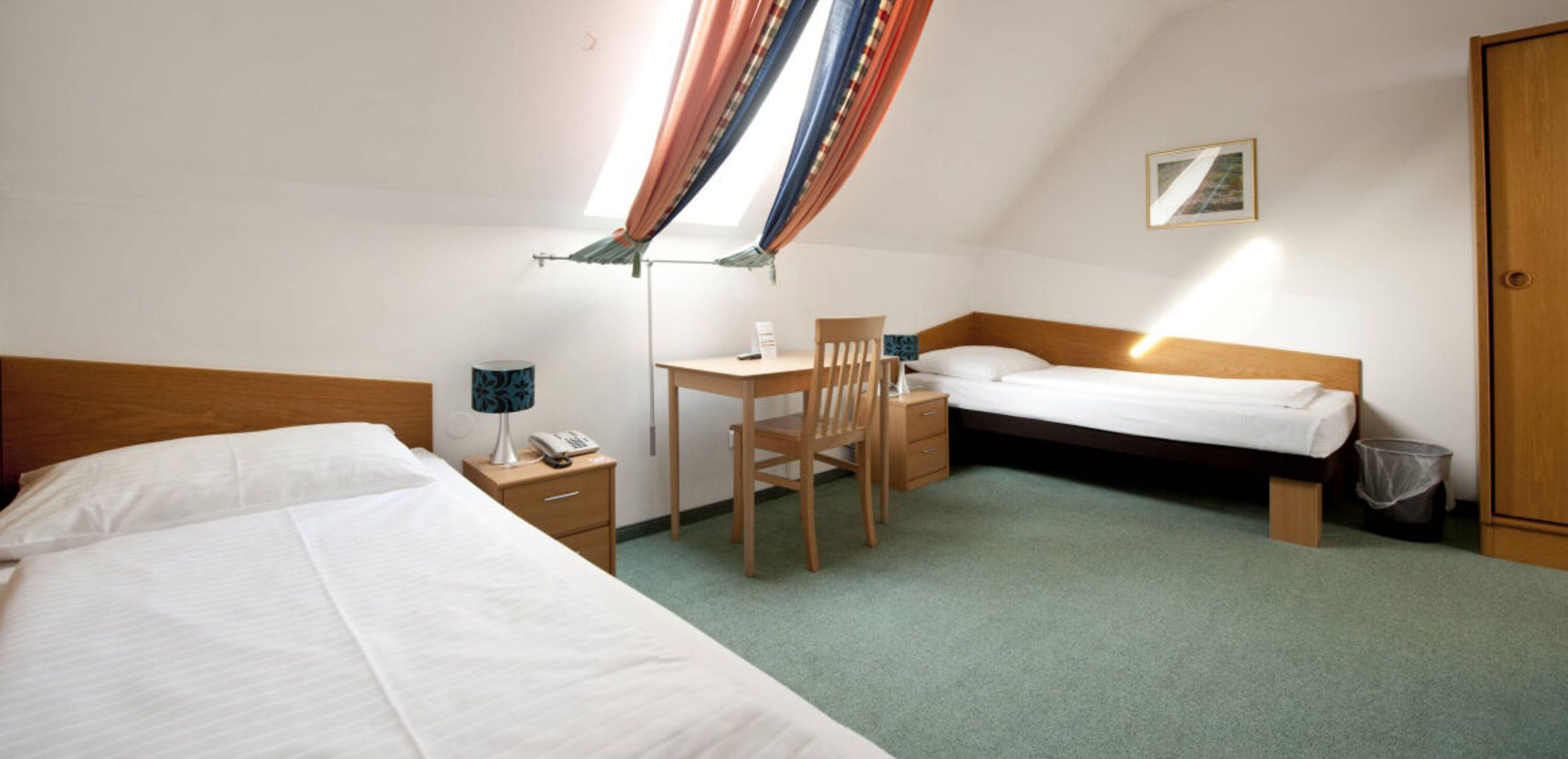 Foto zeigt einfaches Zweibettzimmer mit grünem Teppichboden mit Dachschrägen.