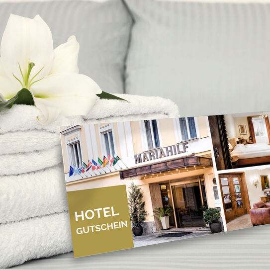 Bild zeigt Hotelgutschein auf einem Bett mit Handtüchern und einer weißen Blume daneben.