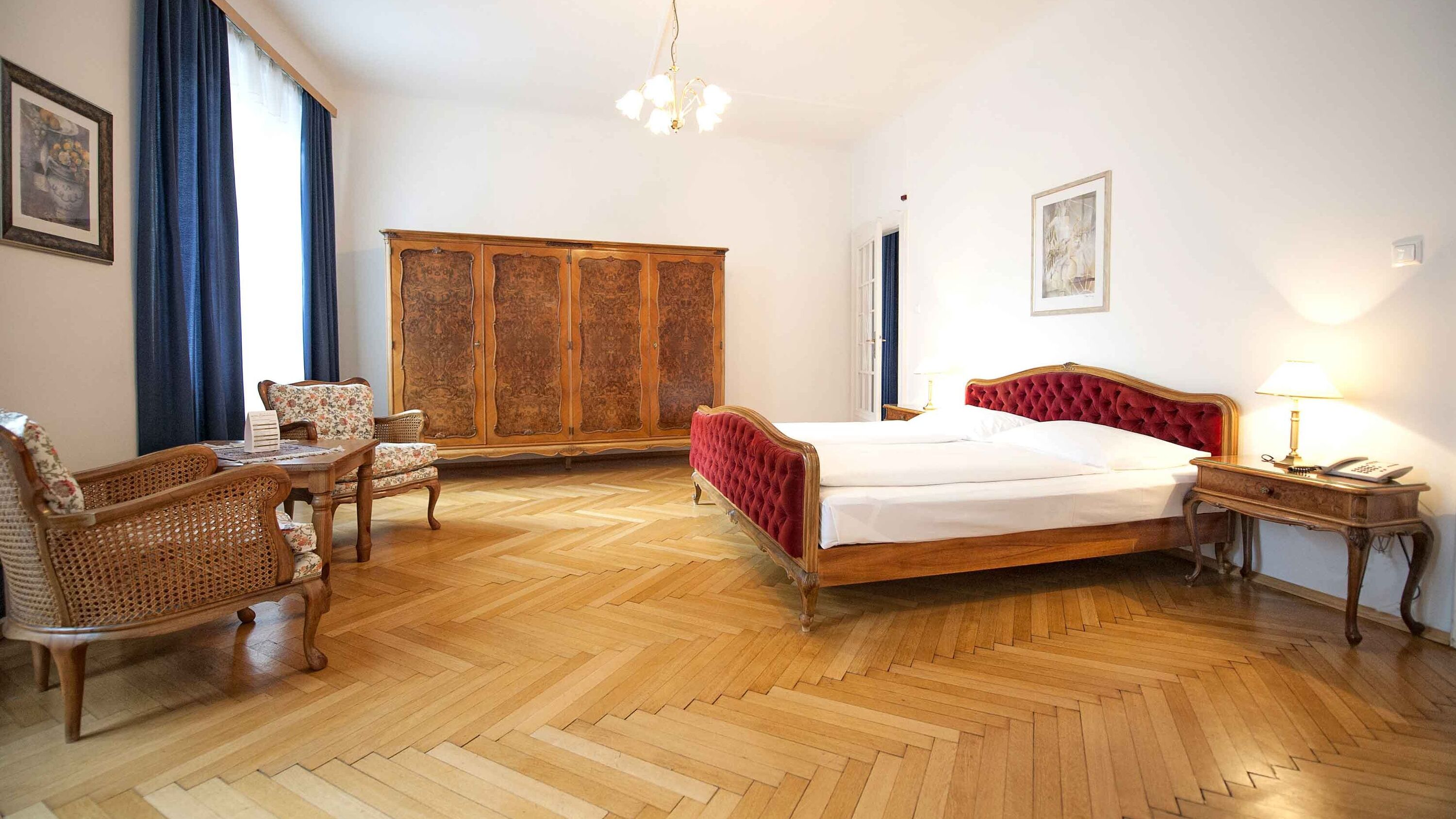 Foto zeigt großzügige Suite mit rotem Samt-Doppelbett und Mobiliär im Jugendstil.