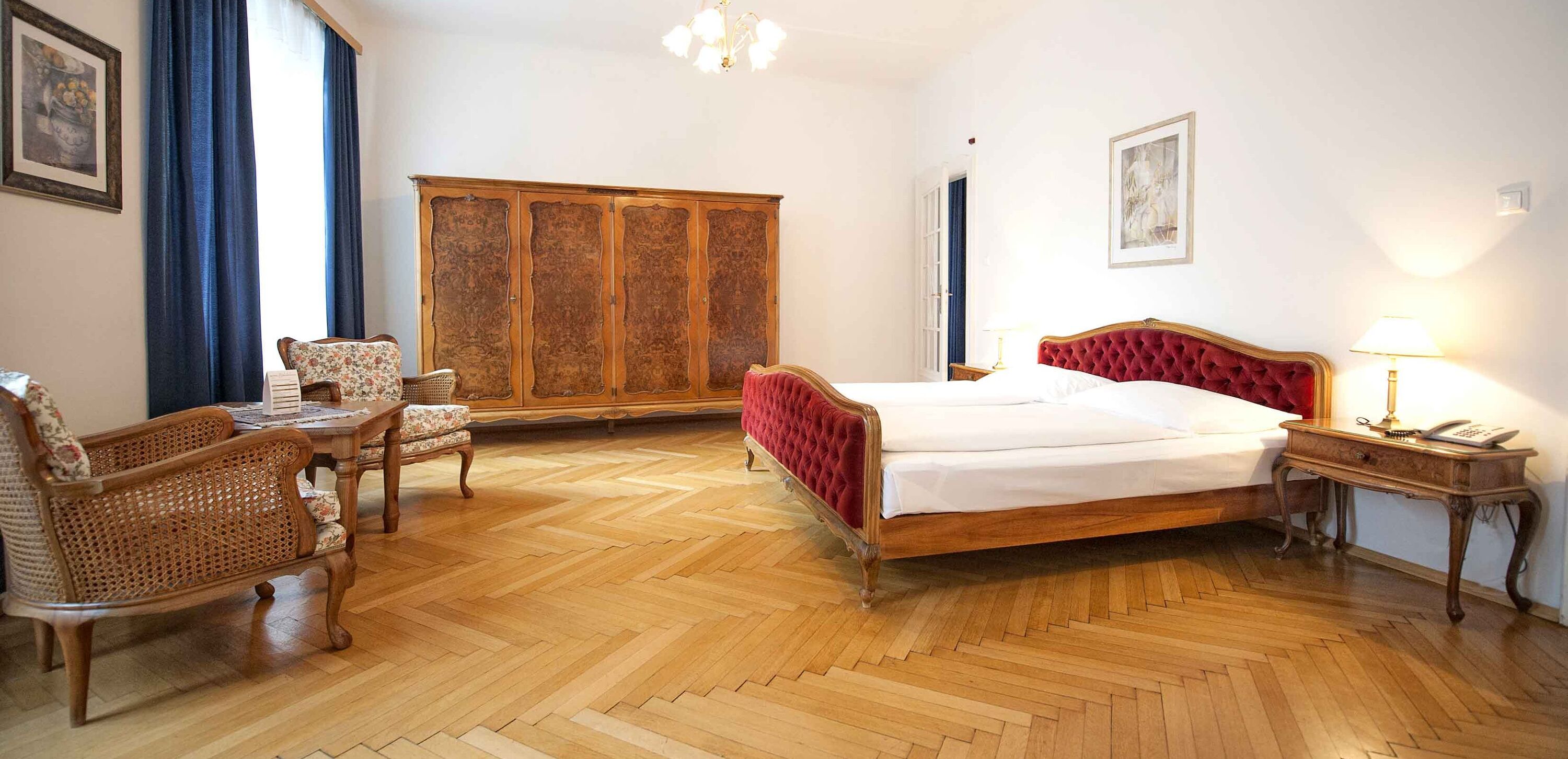 Foto zeigt großzügige Suite mit rotem Samt-Doppelbett und Mobiliär im Jugendstil.